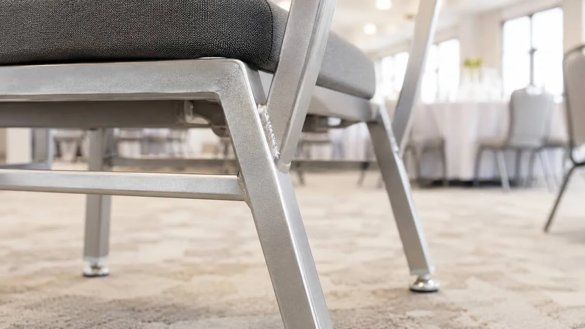 close-up of the frame joint on a commercial-grade steel banquet chair showing the weld quality and glide feet, illustrat