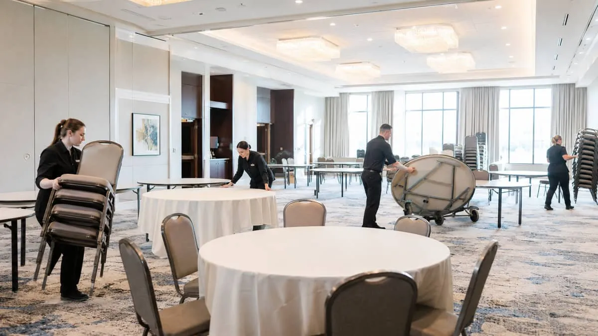 a banquet hall mid-reset with event staff moving chairs and folding tables, showing the practical workflow of a hotel or