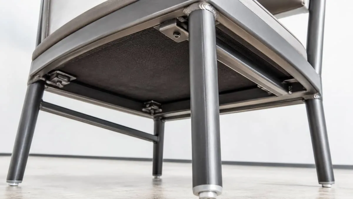 close-up photo of the underside of a contract-grade restaurant chair showing the frame welds, corner blocks, and glide f