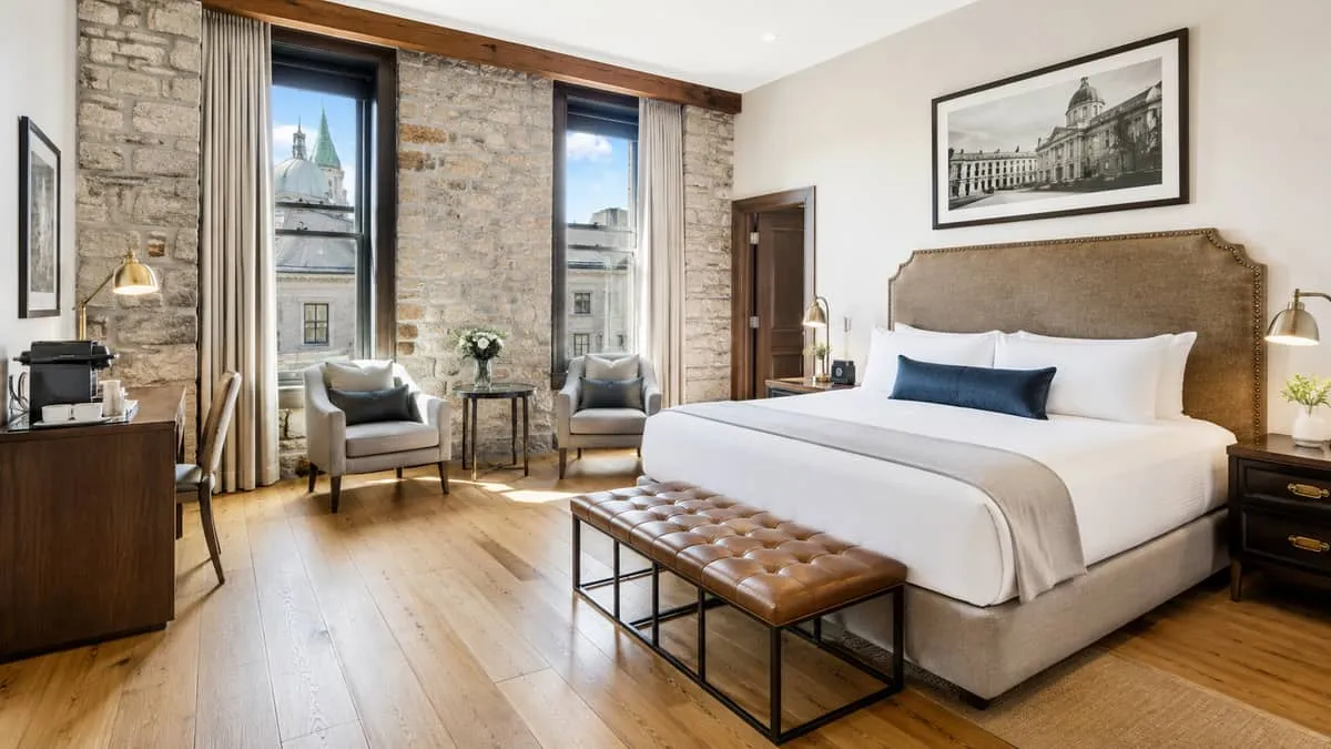 a beautifully furnished boutique hotel room in Old Montreal with exposed stone wall, warm wood flooring, a contract-grad
