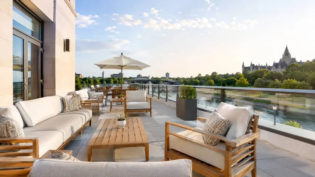 upscale hotel patio in an Ottawa-style setting, showing teak furniture with premium cushions, a canal or green space vie