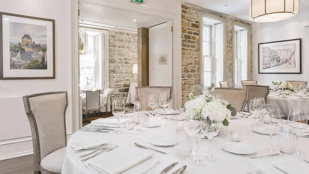 close-up of a set banquet table with upholstered chairs in a warmly lit Quebec City event space, showing white linens, g