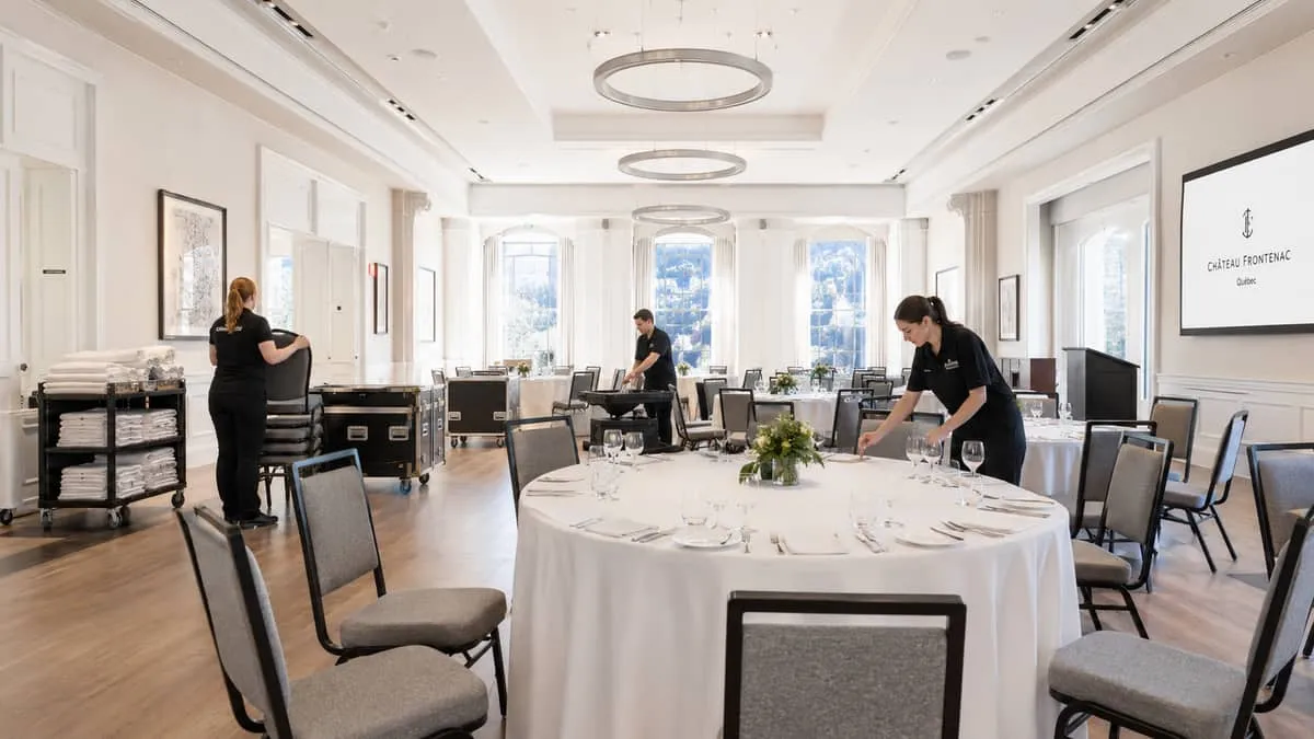 a banquet event setup in progress inside a Quebec City venue, showing staff arranging round tables and chairs with folde