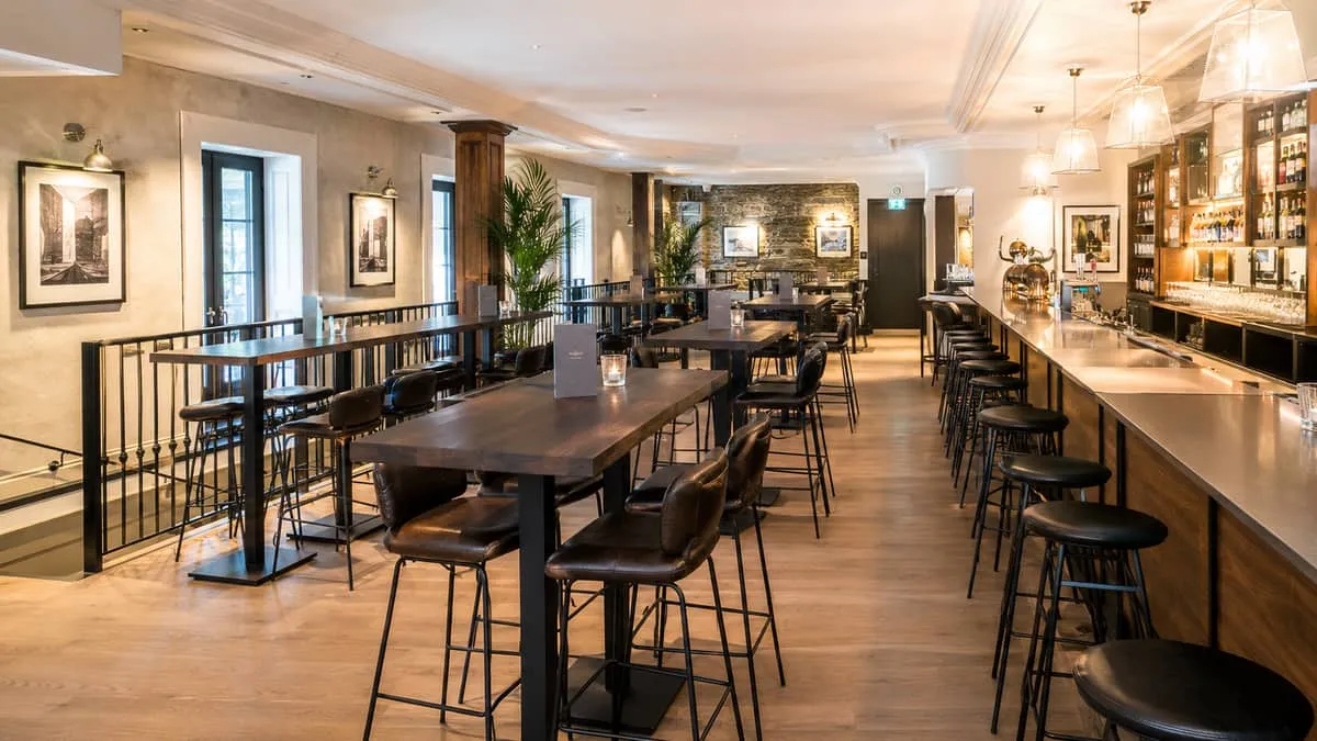 row of commercial high-top tables with metal bases and dark wood tops in a bar setting, showing the layout typical of a 