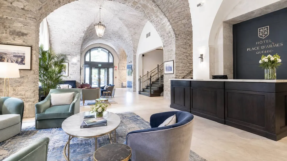 a boutique hotel lobby in Old Quebec with vaulted stone ceilings, French-inspired upholstered armchairs in muted jewel t