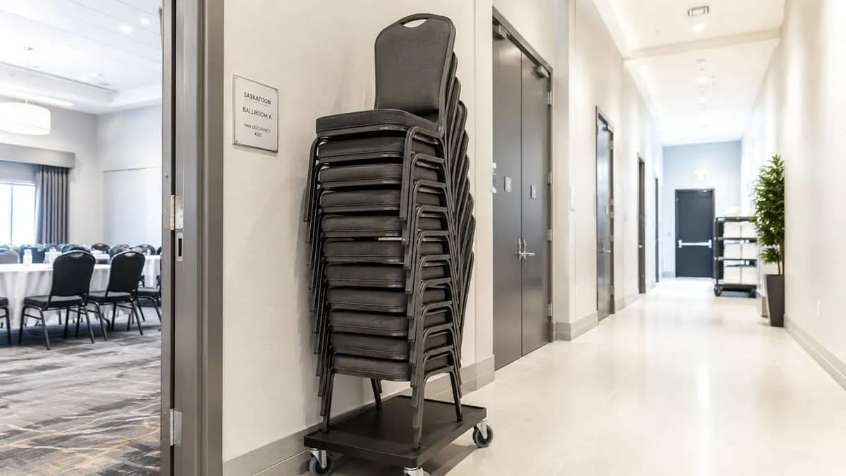 stackable banquet chairs in charcoal or dark grey stacked 10-12 high on a dolly in a storage corridor, showing compact s