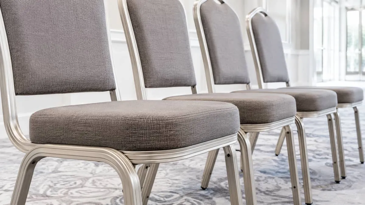 close-up of a row of padded stackable banquet chairs in neutral beige or charcoal fabric, showing clean stitching and le