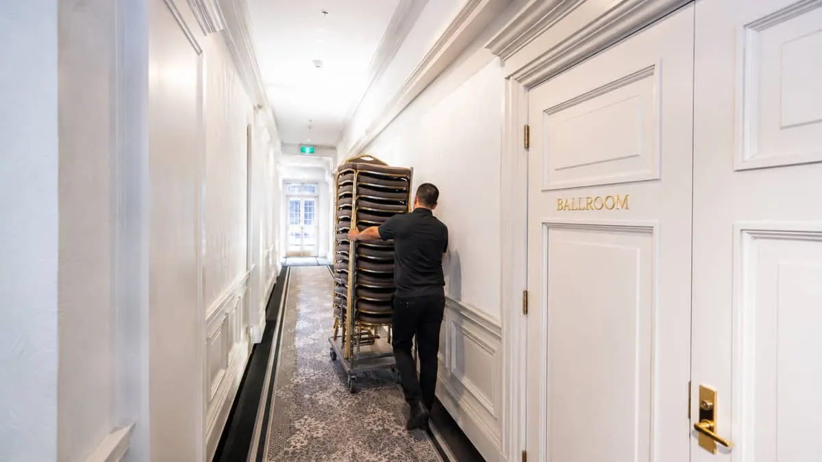 narrow service corridor in a heritage hotel with stacked banquet chairs on a trolley being moved through the hallway, sh