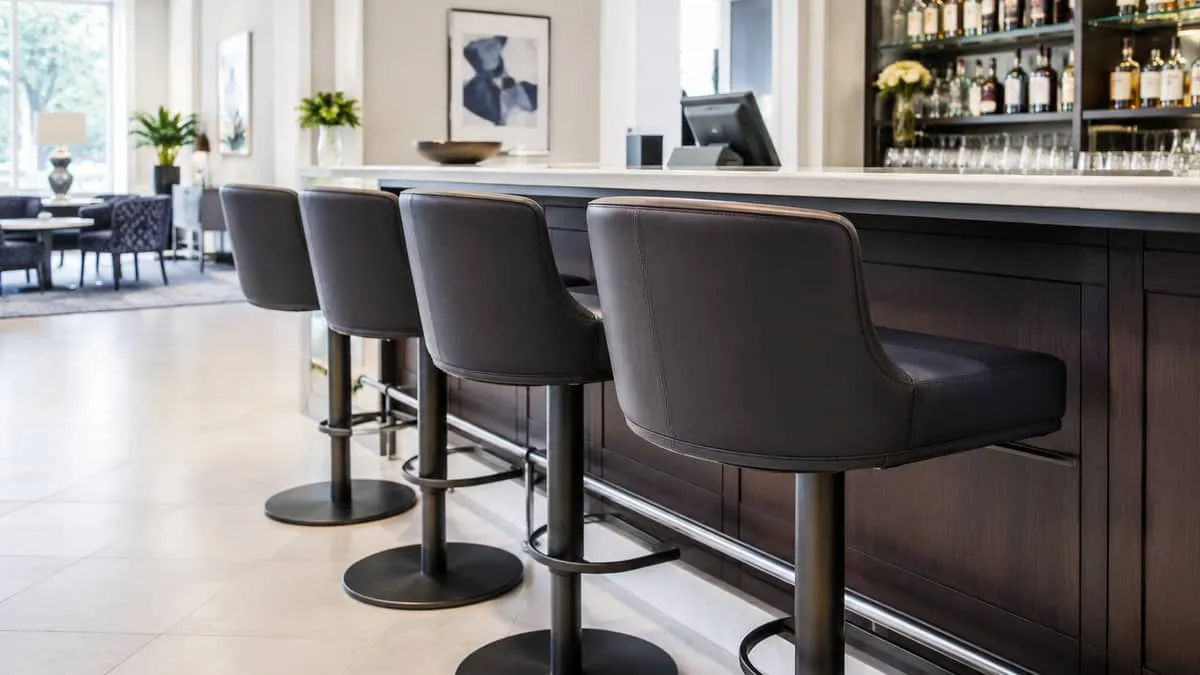 close-up of commercial grade bar stools with upholstered seats in a dark fabric or leather, showing swivel base and foot