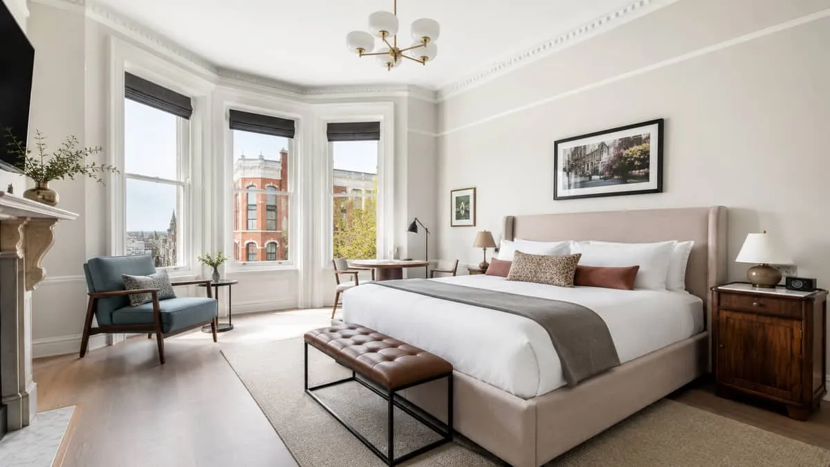 boutique hotel guestroom interior showing a deliberately mixed furniture set: upholstered bed, distinct side tables, a d