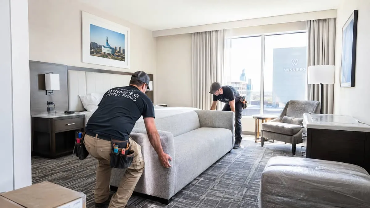 wide shot of a hotel renovation in progress, showing furniture being installed in a guest room or lobby space, with work