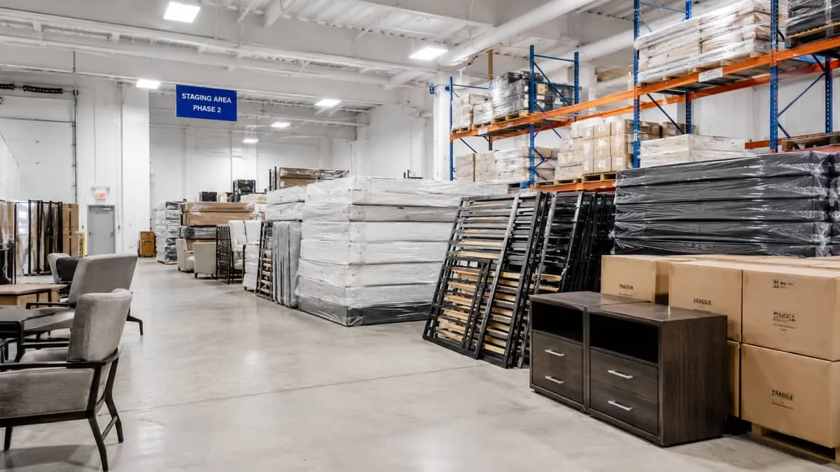 warehouse or staging area showing hotel furniture inventory ready for phased delivery, including stacked bed frames, wra