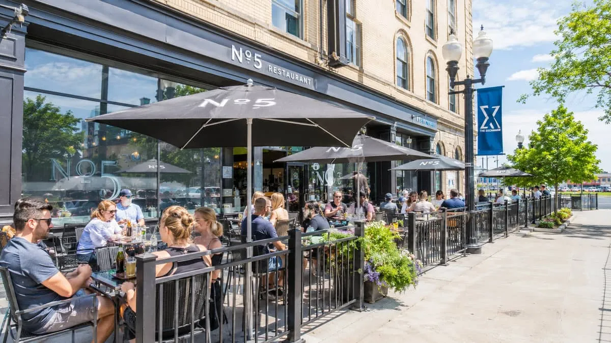 a busy Winnipeg restaurant patio in summer, showing metal-framed commercial chairs and tables with weathered-resistant f